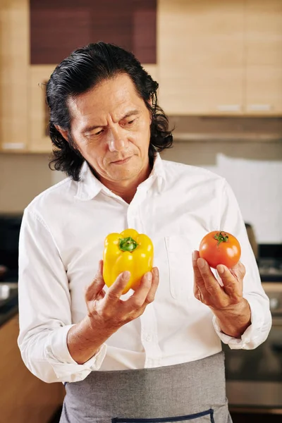 Zamyślony Dojrzały Mężczyzna Patrząc Dojrzałą Organiczną Paprykę Pomidory Dłoniach Stojąc — Zdjęcie stockowe