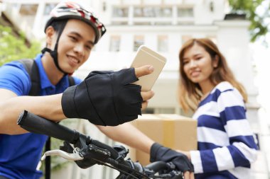 Genç bayana paket teslim ettikten sonra kurye cep telefonu uygulaması üzerinden sonraki adresi kontrol ediyor