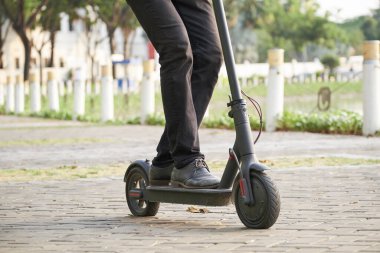 Şehir parkında elektrikli scooter kullanan ve işe gitmek için acele eden genç iş adamının görüntüsü.