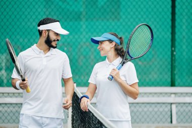 Beyaz üniformalı mutlu genç çift birlikte tenis oynamaktan zevk alıyor.