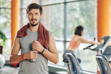 Spor salonundaki eğitimden sonra omzunda havluyla tatlı su içen yakışıklı genç adamın portresi.