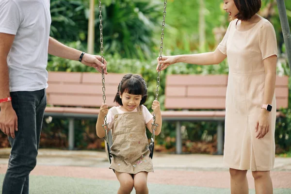 Joven Madre Padre Empujando Hija Swing Mientras Divierten Parque —  Fotos de Stock