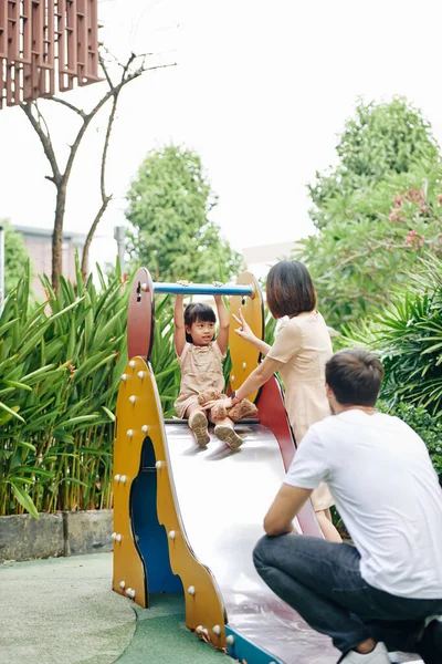 Счастливые Молодые Родители Помогают Своей Дочери Спуститься Детскую Площадку — стоковое фото