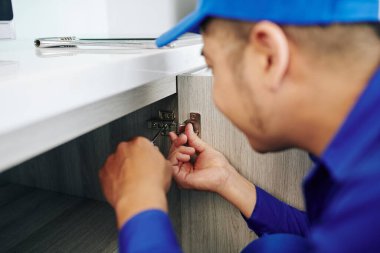 Mutfak mobilyalarını monte eden mavi üniformalı işçinin yakın plan resmi.