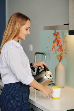 Gülümseyen genç iş kadını mutfak tezgahına sıcak su döküyor.