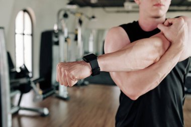 Sporcu spor salonunda ısınırken kollarını açarken akıllı saat takıyor.