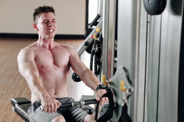 Güçlü, formda bir adam, sıra makinesinde çalışırken dişlerini gıcırdatmaya çalışıyor.