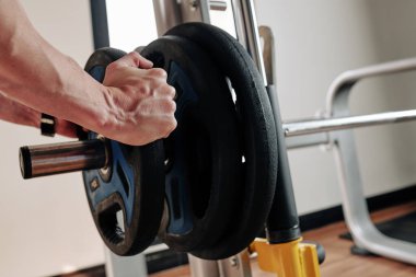 Sporcunun spor salonunda egzersiz yapmadan önce halterlere ağırlık koyduğu yakın plan görüntüsü.