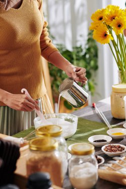 Kadın erimiş sabun malzemelerini cam kaseye boşaltıp yağlar ve renklerle karıştırıyor.