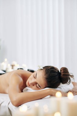 Güzel bir Asyalı kadın sıcak bazalt taşları ve kokulu mumlarla spa ameliyatından zevk alıyor.