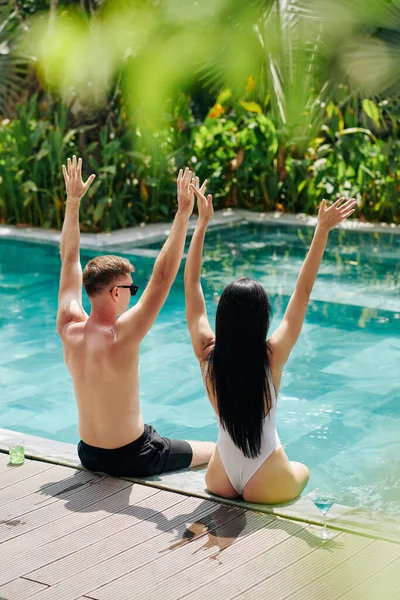 Happy Young Couple Sitting Pool Edge Raising Arms Excitement View — Stock Photo, Image