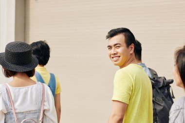 Basit sarı tişörtlü, pozitif Asyalı bir adam üniversiteye gidiyor.