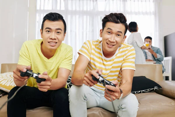 Excited Vietnamese guys playing video games at home, their friends talking in background