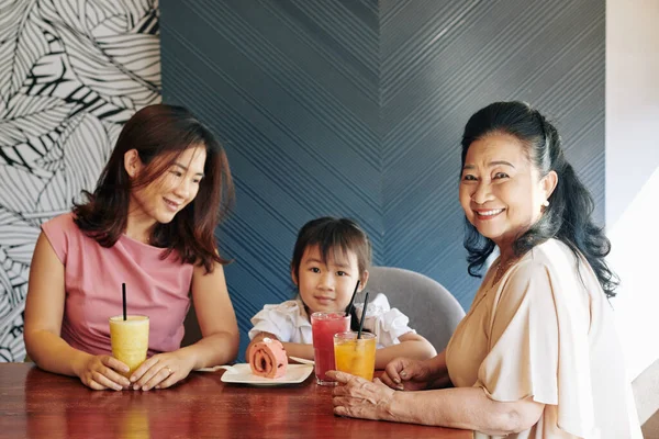 越南母亲和祖母溺爱着可爱的小女孩 送给她美味的水果鸡尾酒和蛋糕 — 图库照片