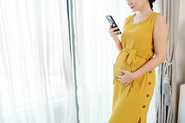 Ung Gravid Kvinna Står Vid Fönstret Och Läser Sms Smartphone — Stockfoto