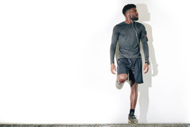 Ciddi bir siyah adam beyaz duvara yaslanıyor ve koşudan sonra dinleniyor.