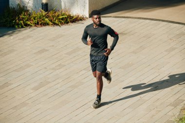 Ciddi bir Afro-Amerikan sporcusu maratona hazırlanırken şort ve acele ile dışarı koşuyor.