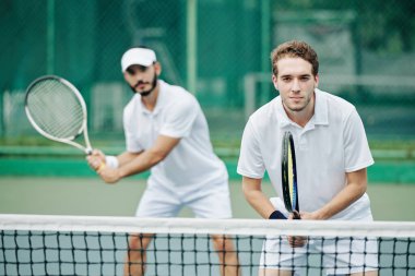 Beyazlar içindeki tenis oyuncularından oluşan ikili takım topa vurmaya hazır.
