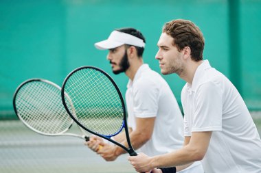 Raketleri oynamaya hazır ciddi konsantre tenis oyuncularının yan görünüşü