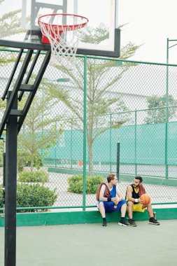 Arkadaşlar dışarıda oturuyorlar, su içiyorlar ve basketbol oynadıktan sonra konuşuyorlar.