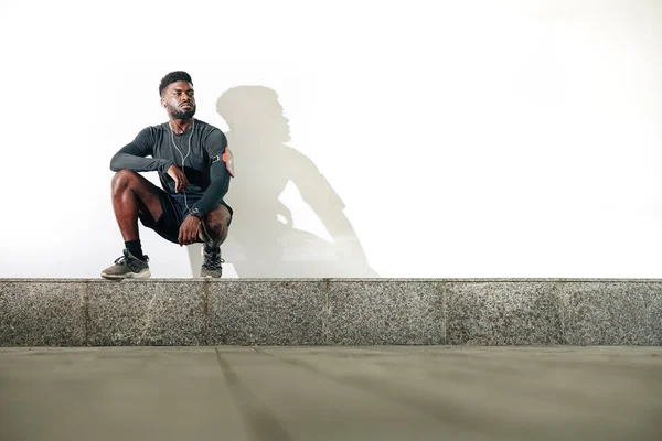 严肃而自信的年轻黑人运动员坐在路边的驼峰上 — 图库照片