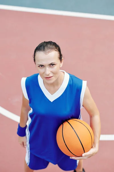 一个严肃的年轻女运动员 拿着篮球在镜头前抬头看 — 图库照片