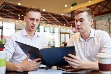Kafede öğle yemeği molası verirken menü okuyan ciddi genç iş adamları.