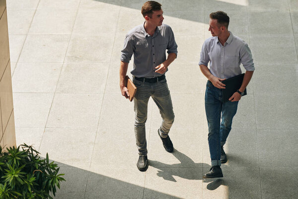 Serious handsome young businessmen walking to office building and discussing project