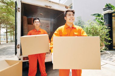 Turuncu üniformalı, eve karton kutular taşıyan Vietnamlı servis elemanları var.