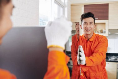 Gülümseyen Vietnamlı taşıma işçileri müşteri mutfağında buzdolabı taşıyorlar.