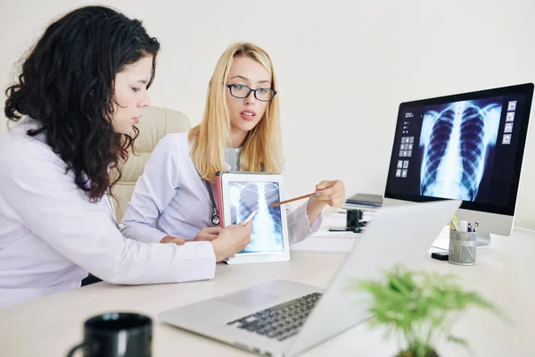 同僚とビデオ会議をしているときにタブレットコンピュータの画面上の肺のX線画像を指している専門の若い女性の肺学者 — ストック写真