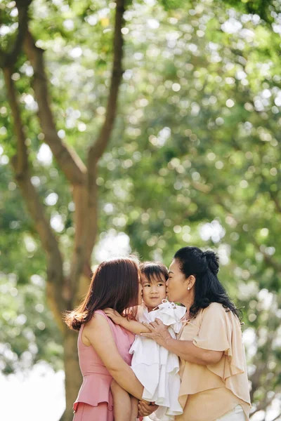 美しいですおばあちゃんとお母さん抱擁とキス女の子で公園に立って — ストック写真