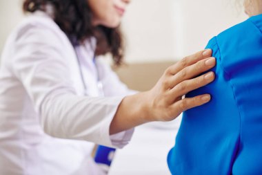 Tıbbi testlerin kötü sonuçları hakkında bilgi verdikten sonra onu rahatlatmak ve desteklemek için yaşlı bir hastanın omzuna dokunan kadın doktor.