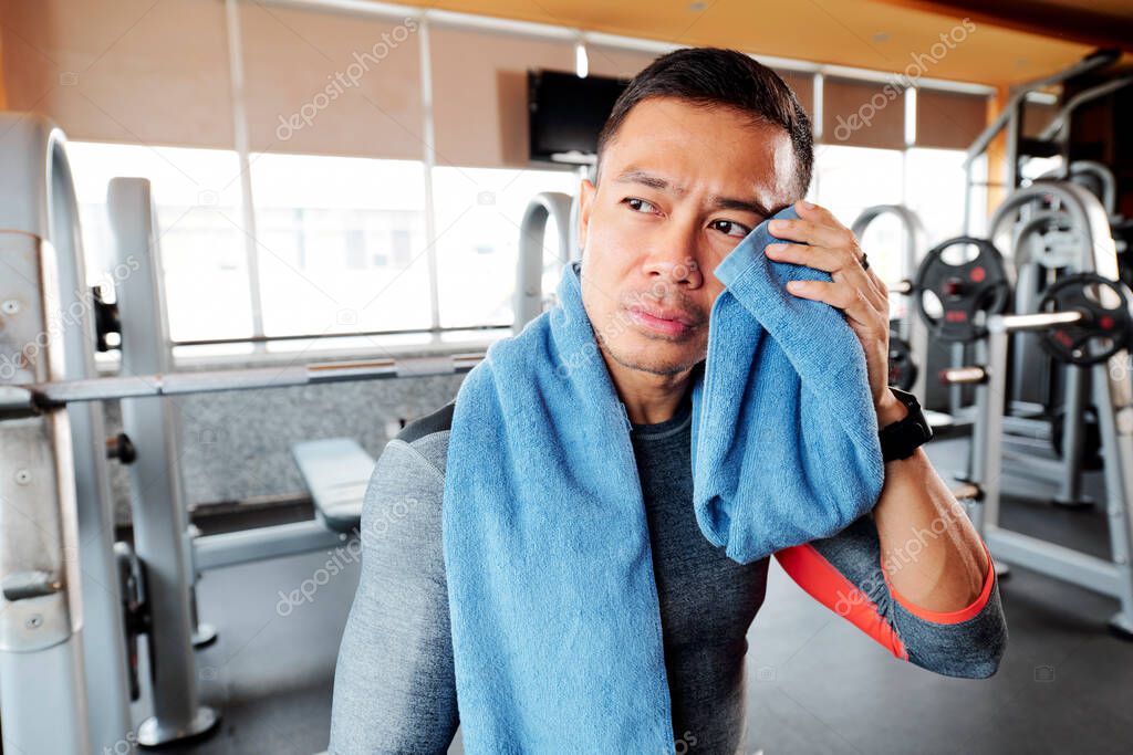 Tired sportsman wiping sweat from his face after lifting heavy barbell in gym