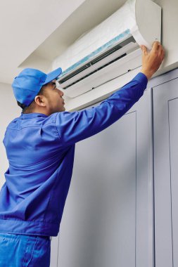 Üniformalı tamirci müşteri evindeki bozuk klimayı kontrol ediyor.