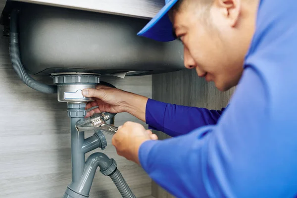 台所で漏れ排水を修復する際にレンチを使用して深刻な配管工 — ストック写真