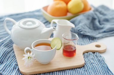Bir bardak lezzetli bitki çayı, limon dilimi ve ahşap dolapta çaydanlık.
