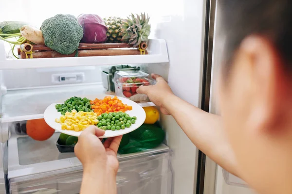 女人从冰箱里拿盘子里的玉米 胡萝卜 青豆和草莓 — 图库照片