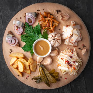 Votka için atıştırmalık bir şeyler. Domuz yağı, kızılcık turşulu lahana, salatalık turşusu, ringa balıklı sandviç, patates kızartması ve mantar turşusundan oluşuyor. Yuvarlak ahşap bir tahtada servis edilmiş. Yukarıdan bak. Gri beton arkaplan