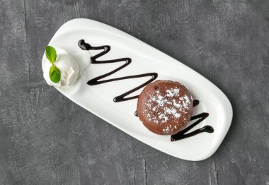 Bir kepçe dondurmalı çikolatalı şekerleme. Nane ve çikolata sosuyla süslenmiş. Beyaz bir tabakta. Yukarıdan bak. Gri beton arkaplan.