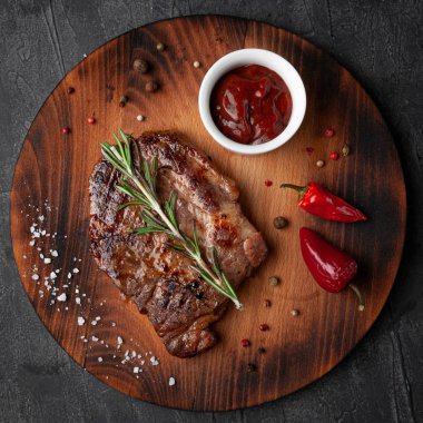 Barbekü soslu domuz eti. Bir tutam biberiye, biber, kaba tuz ve baharatla süslenmiş. Yuvarlak bir tahta üzerinde. Yukarıdan bak. Gri beton arkaplan.