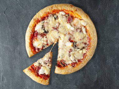 İtalyan pizzası. Av sosisi, peynir, kırmızı biber, mantar, domates, mozzarella peyniri ve domates sosuyla. Pizzadan bir parça kesilir. Yukarıdan bak. Gri beton arka planda. İzole edilmiş.