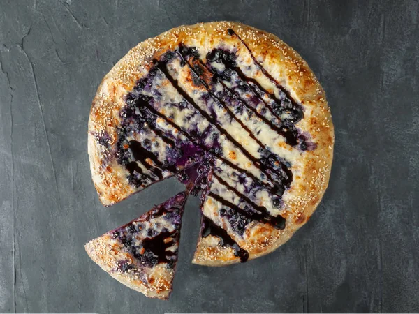 Sweet pizza. blueberries, cream cheese, mozzarella and sulguni, poured with chocolate topping. A piece is cut off from pizza. View from above. On a gray concrete background. Isolated.