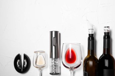 Çelik grisi tirbuşon. Beyaz zemin üzerinde şarap bulunan iki bardak ve şişe. Metin için yer.