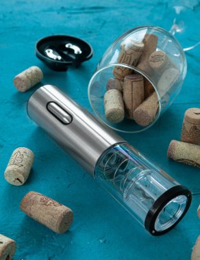 Tirbuşon metalik gri renk. Turkuaz bir arka planda yatıyor. Şarap için bir bardak, havalandırma ve vakum mantarının yanında..