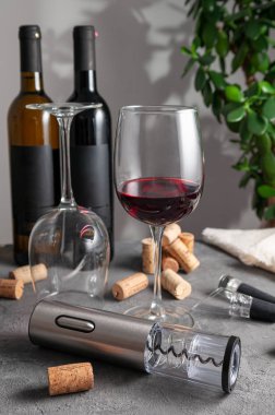 Elektrikli gri metal tirbuşon, havalandırma ve şarap için elektrikli süpürge. Gri beton arka planda. Arka planda iki şişe şarap ve bardak var..