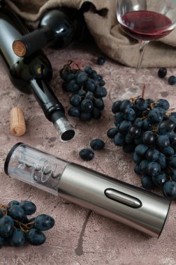 Tirbuşon metalik gri renk. Kahverengi beton bir yüzeyde. Üzüm ve bir şişe şarap.