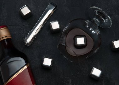 Yeniden kullanılabilir çelik küpler buz simülasyonu yapıyor. Karanlık bir arka planda kürek çekme maşası, viski ve bir şişe