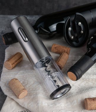 Metalik elektronik kablosuz tirbuşon. Yakınlarda iki şişe şarap ve mantar var. Ahşap ve kumaşın arka planı.