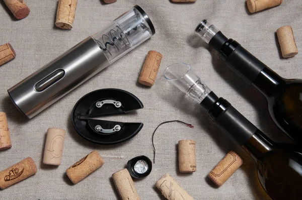 Çelik grisi tirbuşon. Çarşaf arkaplanda yalan söylüyor. Yakınlarda birkaç şarap mantarı ve iki şişe şarap var..